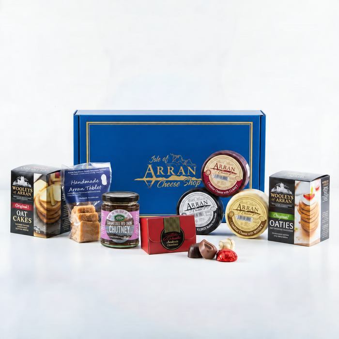 A Fireside Feast Box featuring an Arran cheese gift box surrounded by Wooley’s of Arran oatcakes, tablet, Arran Fine Foods chutney, chocolates, and four round wedges of cheese.