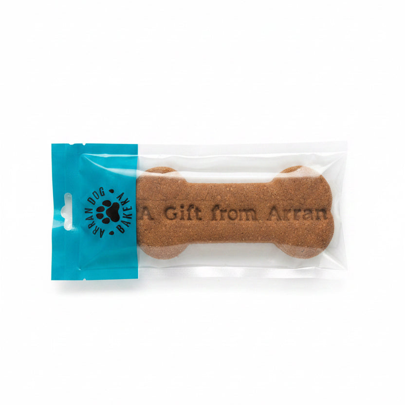 The Handmade Arran Dog Bone Biscuit is a large, natural dog treat shaped like a bone in clear packaging with a blue "Arran Dog Bakery" label. "A Gift from Arran" is printed on the biscuit.