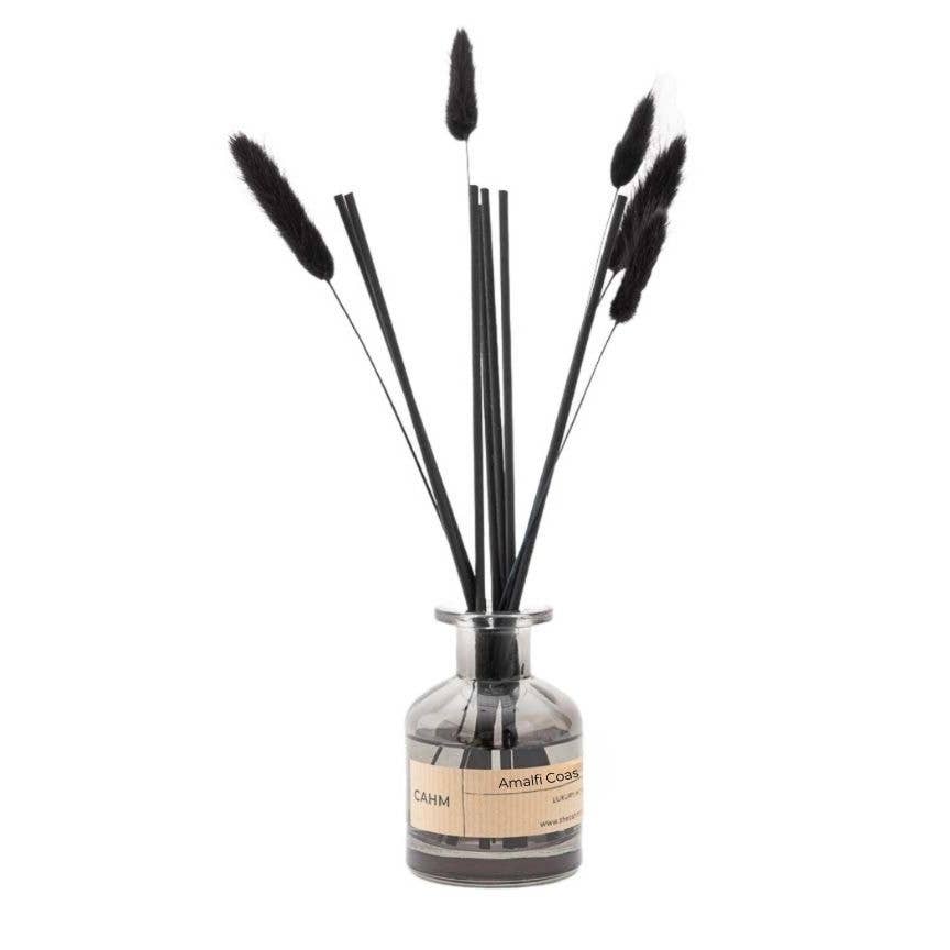 The Amalfi Coast Reed Diffuser Black is a stylish home decor piece featuring a glass bottle with long black reeds and pampas grass, exuding premium fragrance oil to evoke the essence of the Amalfi Coast.