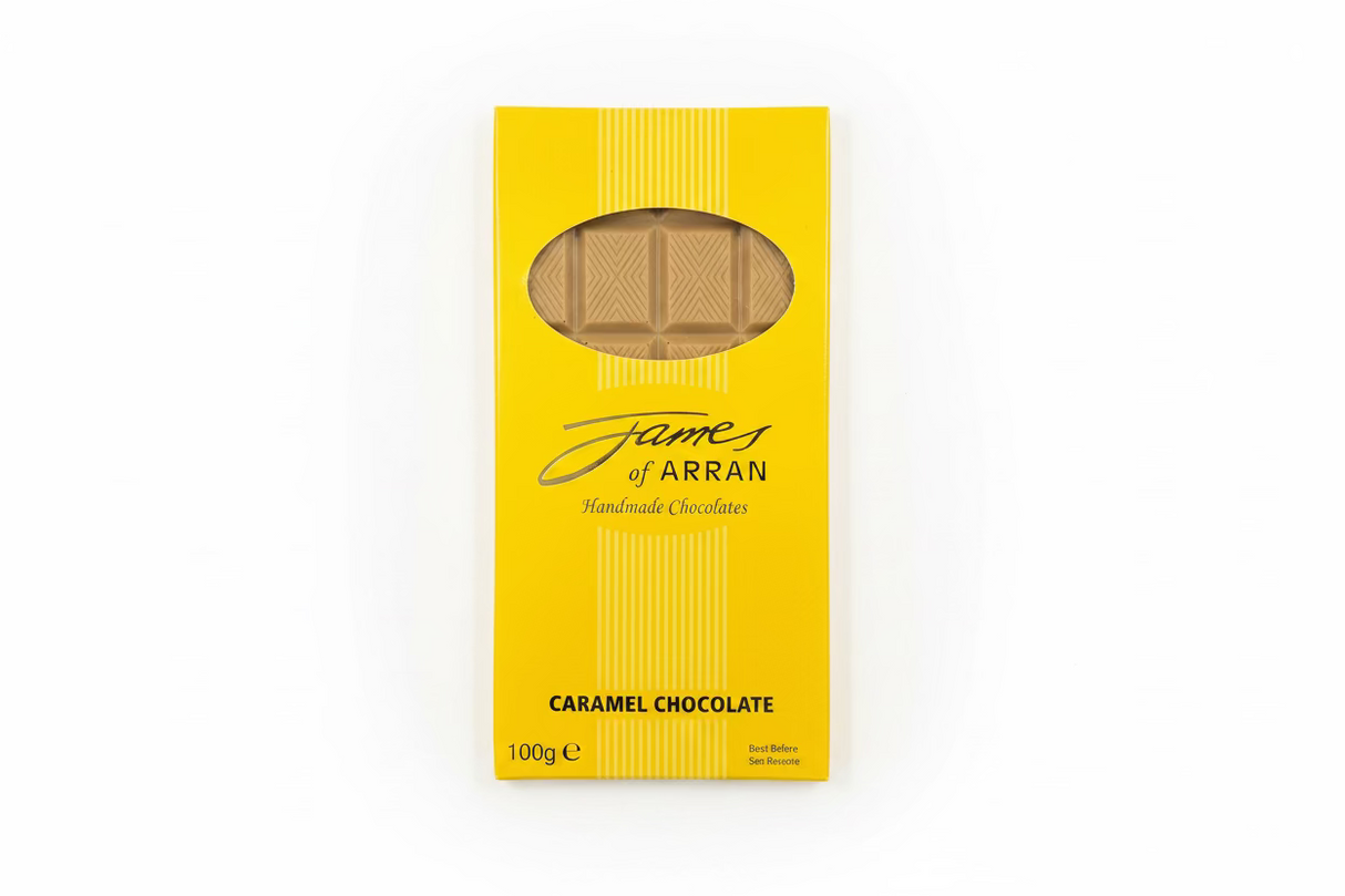 A yellow box labeled "James Chocolates Luxury Bar of Caramel Chocolate" displays visible caramel chocolate pieces through a clear window. The packaging indicates a weight of 100 grams, resembling an enticing caramel chocolate bar, elegantly placed on a dark surface.
