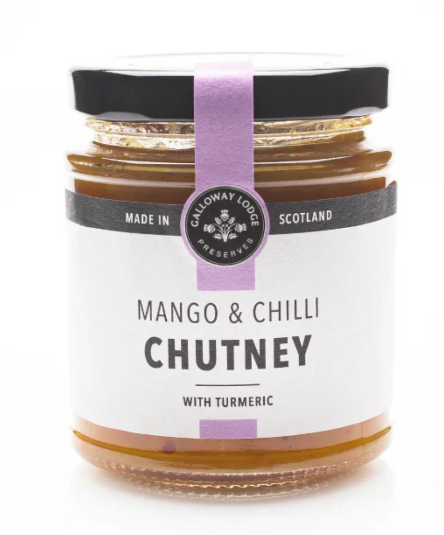 A glass jar of Mango and Chilli Chutney with turmeric, ideal for cheeseboards. The jar has a black lid, a purple ribbon, and a white label with black text.