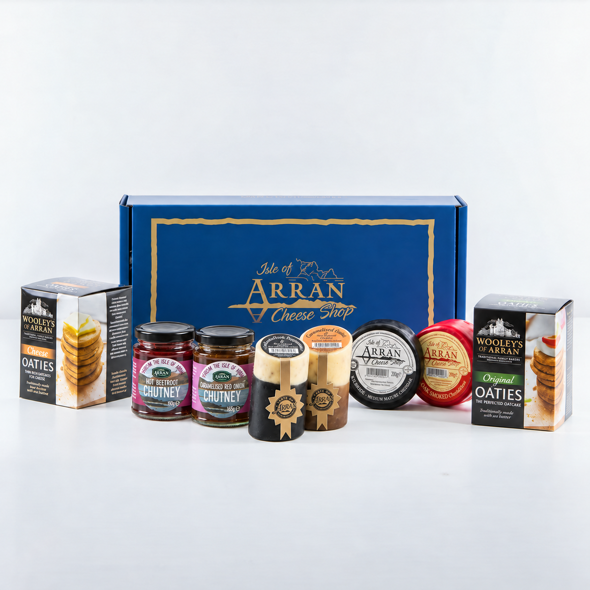 A Cheese Lover Hamper featuring a gift box behind two boxes of oatcakes, two jars of chutney, and four rounds of Arran cheddar.