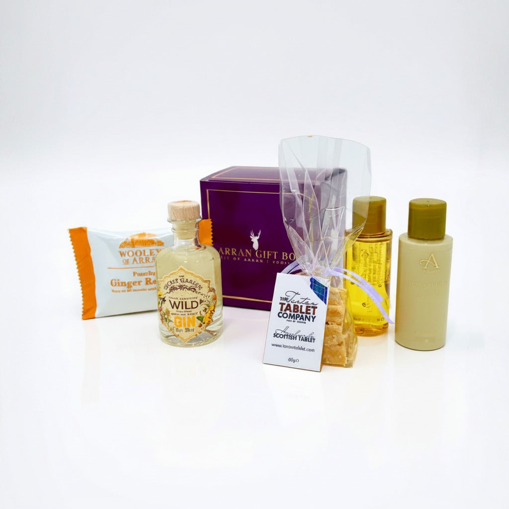 The Wee Goatfell Gift Box features a ginger soap bar, Secret Garden Organic Wild Gin mini, tablet sweets, toiletries, and a purple Isle of Arran Scottish gift box—all beautifully arranged on a white background.