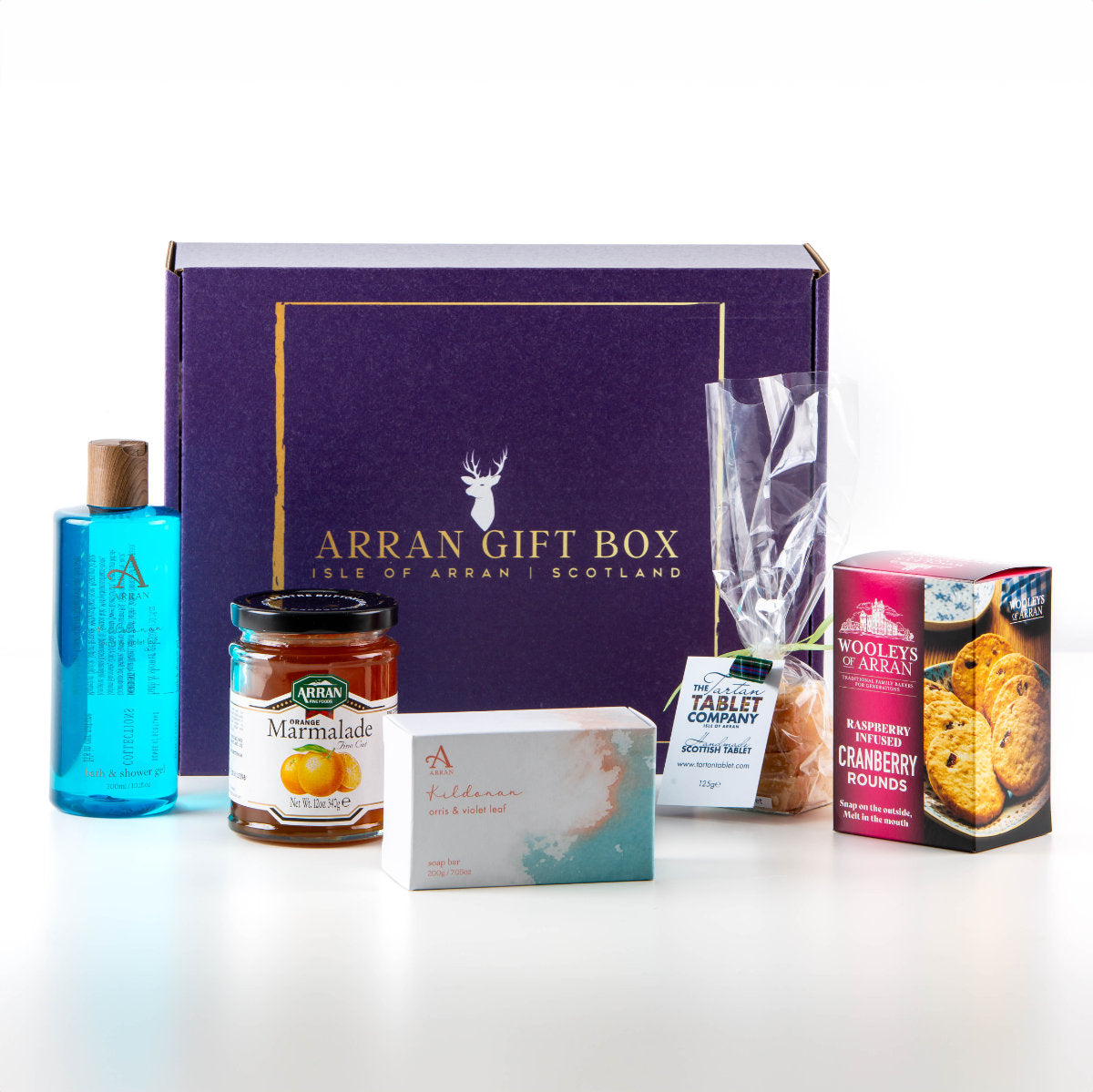 A purple box labeled "Arran Gift Box" is surrounded by various items: a blue bath/shower gel, a jar of marmalade, a small box of fudge, a packet of oatcakes, a small box of cranberry rounds, and a chocolate bar.