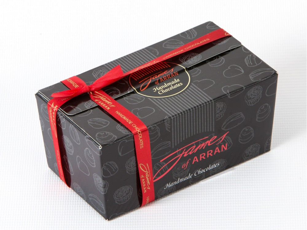 A rectangular black gift box of James of Arran Handmade Chocolates, decorated with a red ribbon and featuring gold and red lettering on the packaging.