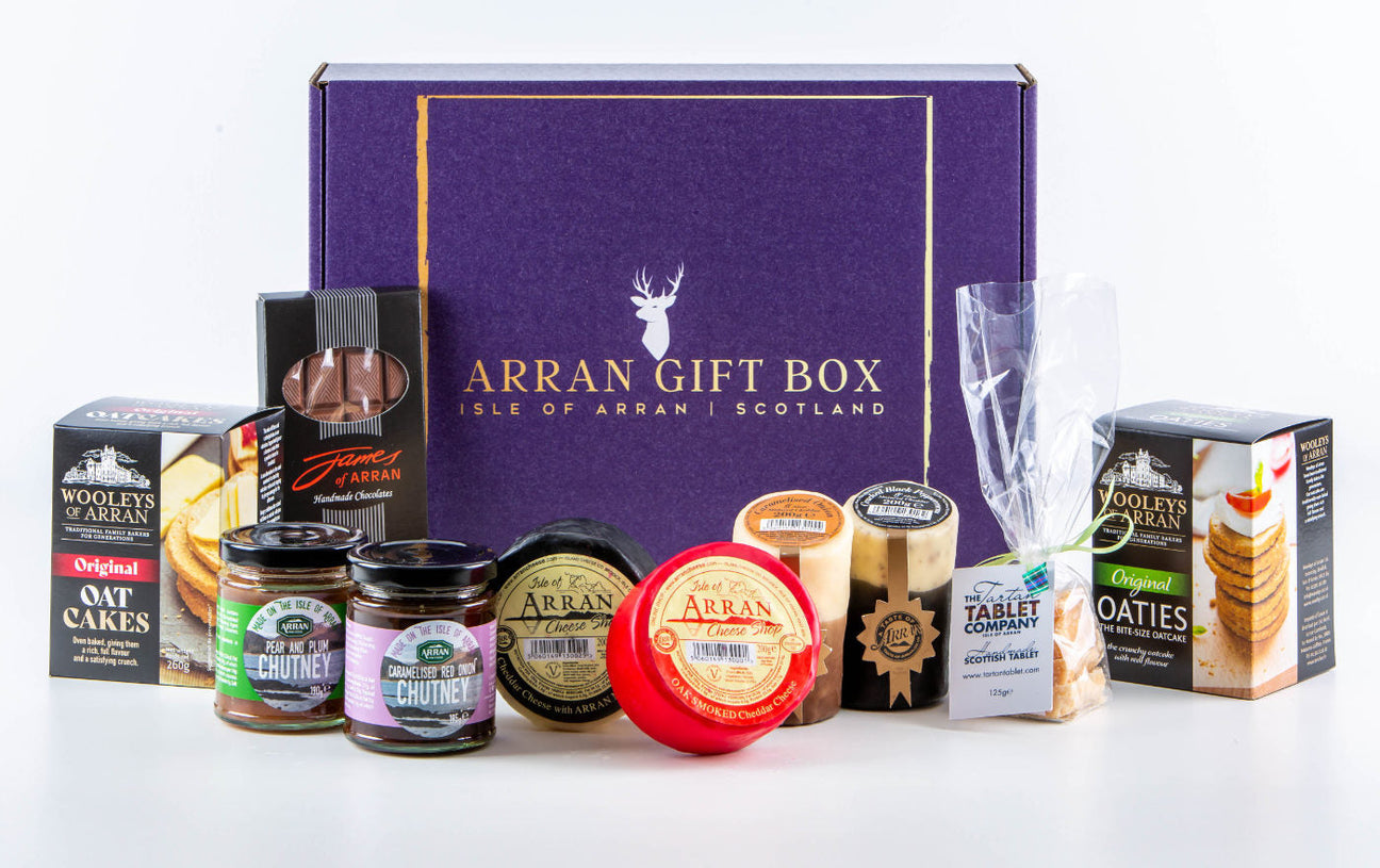 A selection of Scottish treats in front of a purple "Arran Gift Box" with oatcakes, chutneys, cheeses, and a chocolate assortment.