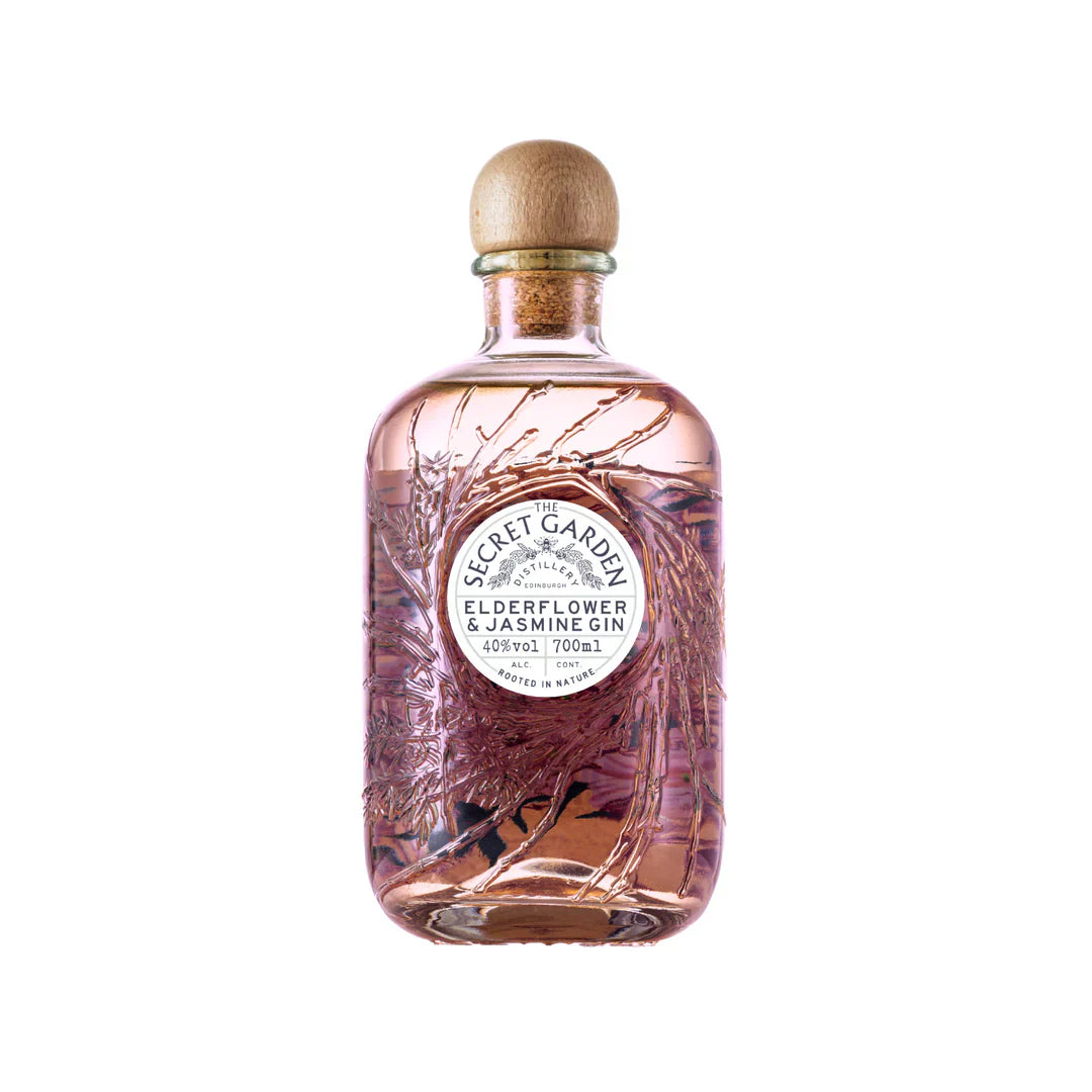 A clear glass bottle of Secret Garden Elderflower & Jasmine Gin with a wooden cap, pink liquid inside, and embossed botanical designs on the glass. The label is white with black text.