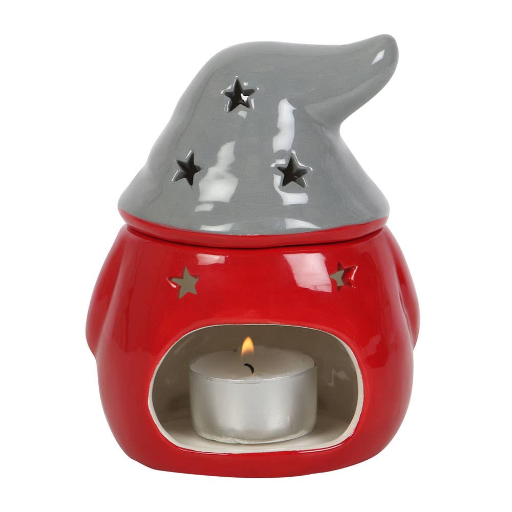 Ceramic candle holder shaped like a gnome with a red body and gray hat featuring star cutouts. A small lit candle sits inside.