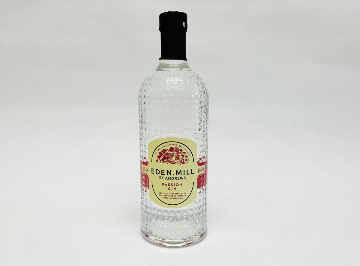 A clear glass bottle of Eden Mill St Andrews Passion Gin with a textured surface and a black cap. The label is white with red accents and features a decorative floral design.