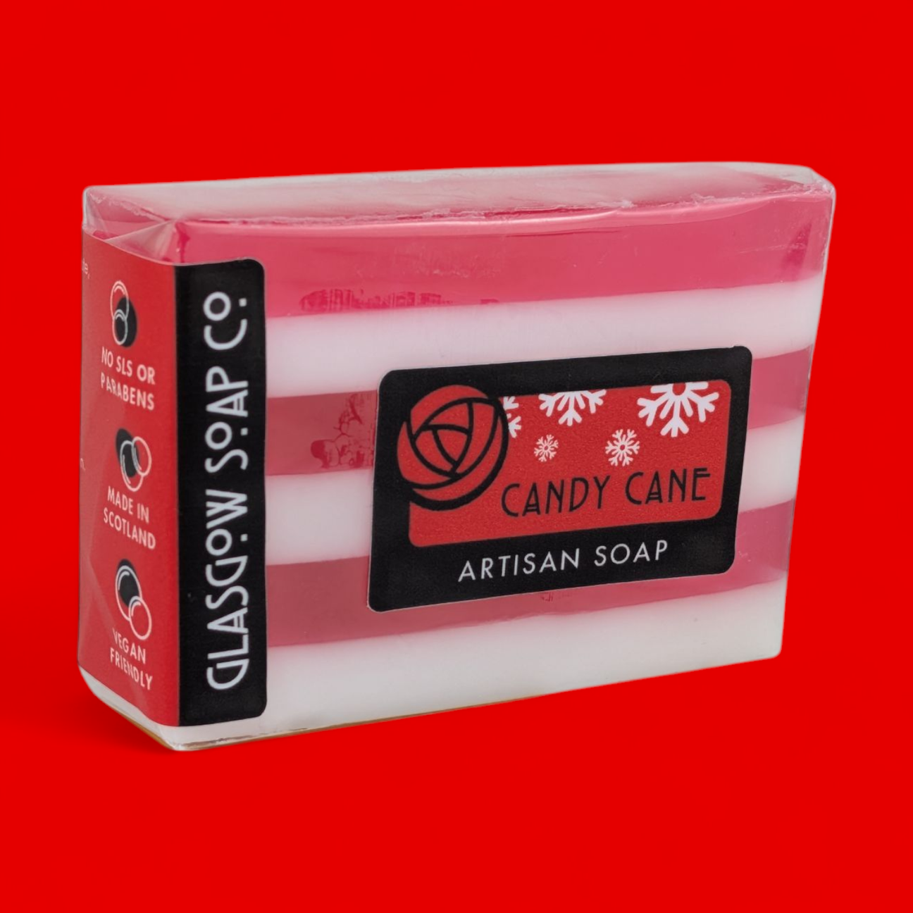 A bar of Glasgow Soap Co. artisan soap labeled "Candy Cane" with red and white stripes, wrapped in plastic packaging, set against a bright red background.