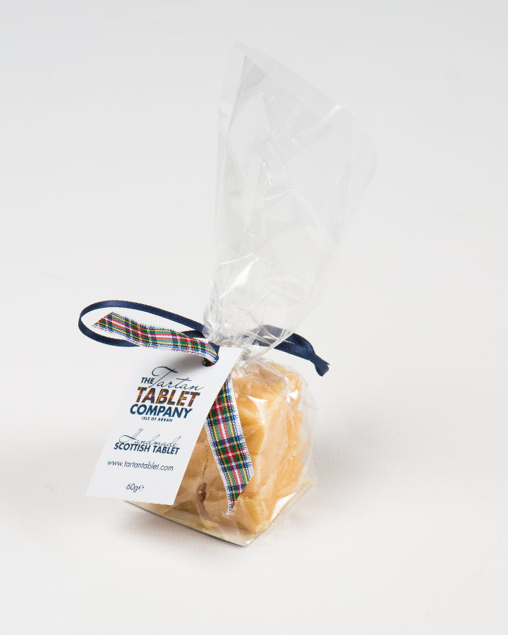 A clear bag of Scottish tablet tied with a blue tartan ribbon, featuring a label from The Tobermory Tablet Company on a plain white background.