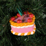 A Heart, Heart Cake ornament with pink frosting, white trim, and red cherries hanging on a Christmas tree.