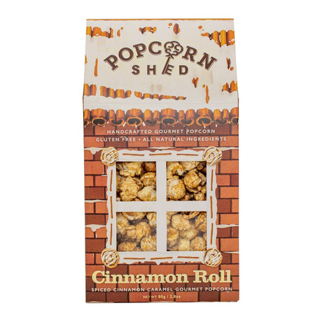 A box of Cinnamon Roll Popcorn Shed, handcrafted in the UK and featuring a charming brick house design with a window displaying delicious caramel popcorn, highlights that it is gluten free, all natural, and boasts a spiced cinnamon caramel flavor.