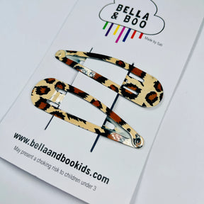 Add a touch of style with Leopard Print Snap Clips—two modern hair clips on a white "BELLA & BOO" card featuring a cloud logo, colorful stripes, and website details. Perfect for chic hair accessorizing.