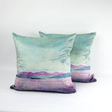 Two Arran Velvet Cushions with a soft watercolor-style landscape in pastel green, purple, and pink, featuring mountains and water, showcase contemporary Scottish design against a plain white background.