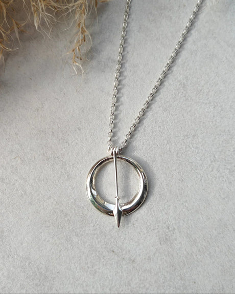 The ‘Sacred Empress’ Necklace, crafted in sterling silver with a handcrafted arrow-inspired pendant, is elegantly displayed on a light gray textured surface.