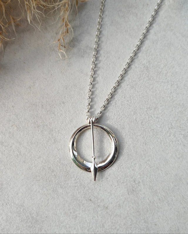 The ‘Sacred Empress’ Necklace, crafted in sterling silver with a handcrafted arrow-inspired pendant, is elegantly displayed on a light gray textured surface.