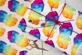 A gift wrapped in Arran Watercolour Map Gift Wrap, tied with red string and topped with dried flowers, sits beside vintage scissors on a matching patterned surface.