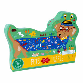 Introducing the Pets 20pc “Sausage Dog” Shaped Jigsaw with Shaped Box—a dog-shaped box featuring a vibrant illustration of a sausage dog wearing glasses, a hat, and an animal-patterned sweater. This playful puzzle includes 20 chunky pieces, perfect for little hands. The box displays colorful text that reads “Floss & Rock Pets Puzzle.”.