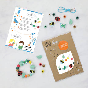 The “Make Your Own Minibeast Bracelet” kit is a children’s bracelet craft set featuring colorful beads shaped like insects and leaves, displayed with an instruction card and brown packaging labeled “Minibeasts Bracelet” on a white surface. This plastic-free kit includes all the tools needed to create a charming bug-themed bracelet—ideal as a party favour. The completed bracelet and included tools are also shown.