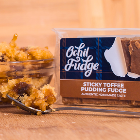 A pack of Sticky Toffee Pudding Fudge sits beside a bowl of sticky toffee pudding, with a fork holding a bite of the homemade fudge dessert in the foreground.