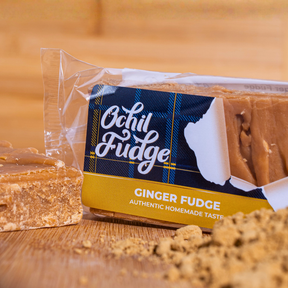 A partially opened package of Ginger Fudge sits on a wooden surface, revealing handmade fudge and scattered crumbs. The label says "Ginger Fudge: Authentic Homemade Taste." Enjoy classic Scottish flavor.