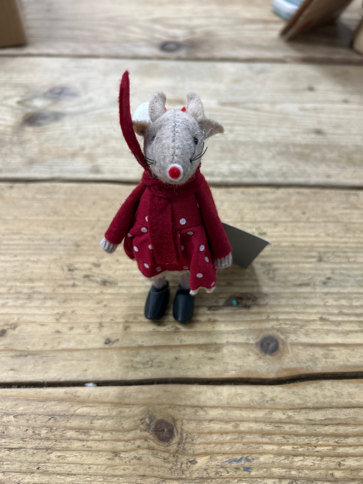 A small “Mouse with Polka Dot dress” stuffed toy, dressed in a red coat adorned with white polka dots and black shoes, stands on a wooden surface.