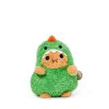 A small, plush toy with a round, orange face and paws, dressed in a fluffy green dinosaur costume featuring a tiny orange spike and white teeth on the hood, sits on a white background. The adorable Noodoll Ricespud Dinosaur is perfect for cuddling.