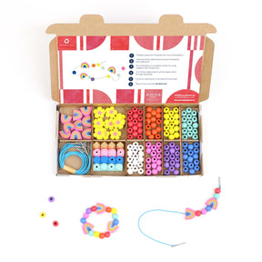 An open box displays vibrant wooden beads, cords, and instructions for creating jewelry with the Rainbow & Flower Bracelet Making Kit. Finished bracelets and individual beads are arranged outside the box, making it an ideal choice for creative play or as unique party favours.