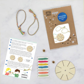 Make Your Own Friendship Bracelet Kit—with instruction sheet, colored threads, wooden disk, wooden beads, and two finished bracelets neatly displayed on a white surface—is a plastic-free craft kit that makes an ideal party favor and inspires creative fun for all ages.