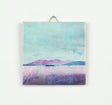 The Arran over Sound of Bute Gift Boxed ceramic art print features a serene lake, small islands, and distant purple mountains beneath a cloudy blue sky, beautifully presented in a ceramic tile and ready to display.