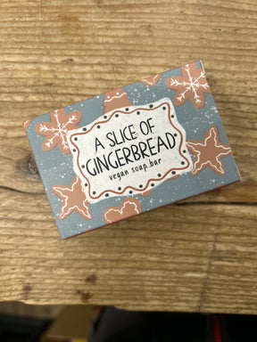 A rectangular box of "A slice of gingerbread vegan soap bar" featuring gingerbread cookie images on a blue and brown background sits on a wooden surface.