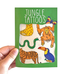 A hand holds a green packet labeled "Jungle Animal Transfer Tattoos," featuring quirky tattoos of a snake, tiger, toucan, orangutan, butterfly, and cheetah—making it a fun and unique gift option.