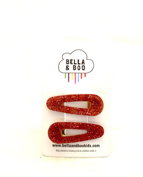 A set of two Red Glitter Hair Clips on a white "BELLA & BOO" card with a cloud logo and rainbow lines. Fun festive accessories for kids, with "www.bellaandbookids.com" at the bottom.