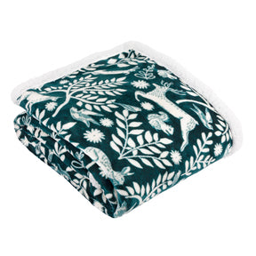 The Skandi Woodland Sherpa Fleece Throw Forest (140 x 180cm) is a dark green blanket with a white sherpa lining, featuring a woodland design of white flowers, leaves, cats, and birds.