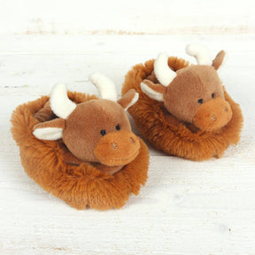 The Jomanda Highland Cow Plush Baby Soft Slippers are cozy brown house shoes with plush horns, ears, and embroidered faces. Doubles as a soft toy—makes a perfect baby gift. Shown on a white wooden surface.