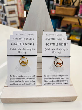 Display of Goatfell Wish Bracelets featuring mountain-shaped charms on cards that say, “Celebrate climbing to the top!” Each includes a poem inspired by Goatfell on Arran, serving as a motivational symbol.