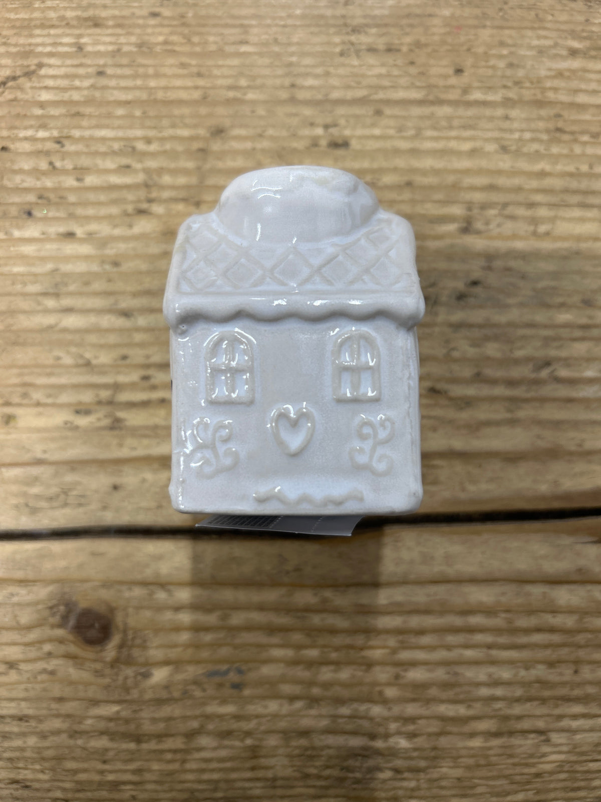 A Ceramic candlestick - 6cm white gingerbread house, featuring decorative windows and a heart design, sits on a wooden surface.