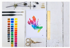 A colorful watercolor paint chart, three paintbrushes, an abstract rainbow painting, art supplies, and a Skye Map Print A5 by Sarah Leask Studio are arranged on a white wooden surface.