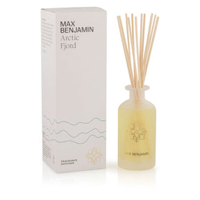 The Max Benjamin Arctic Fjord Diffuser features a frosted glass bottle with yellow liquid, wooden reeds, and a white box in minimalist teal and gold for an elegant, long-lasting home fragrance made with natural essential oils.
