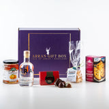 A purple Gin Treat Scottish Gin Box 20 cl, featuring Secret Garden Organic Elderflower & Jasmine Gin, is displayed with Scottish artisan treats: orange marmalade, assorted chocolates, tablet candy, fudge, and cranberry rounds.