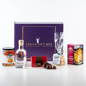 A purple Gin Treat Scottish Gin Box 20 cl, featuring Secret Garden Organic Elderflower & Jasmine Gin, is displayed with Scottish artisan treats: orange marmalade, assorted chocolates, tablet candy, fudge, and cranberry rounds.