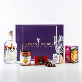 The Deluxe Gin Treat Box 70cl featuring Secret Garden Organic Wild Gin is displayed with Isle of Arran treats: marmalade, chocolates, fudge, cranberry rounds, Scottish tablet, and a purple gift box with gold lettering.