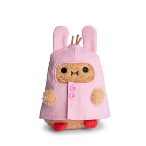 A cute Noodoll Ricespud Bunny Boot Pink Raincoat plush toy, shaped like a small animal, wears a pink hooded raincoat with bunny ears and pink buttons. It features small red feet and fuzzy beige paws, making it perfect for cuddling or display against a white background.