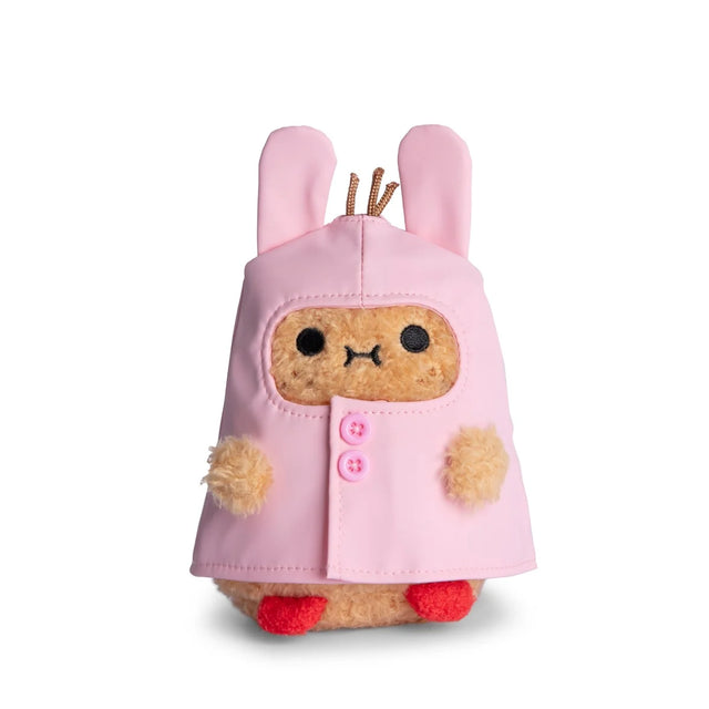 A cute Noodoll Ricespud Bunny Boot Pink Raincoat plush toy, shaped like a small animal, wears a pink hooded raincoat with bunny ears and pink buttons. It features small red feet and fuzzy beige paws, making it perfect for cuddling or display against a white background.