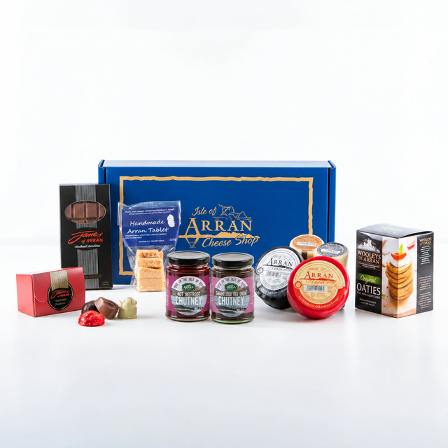 A Best of Arran gift box surrounded by assorted artisanal products including handmade chocolates, fudge, beetroot and onion chutneys, several rounds of cheese, and a box of oatcakes.