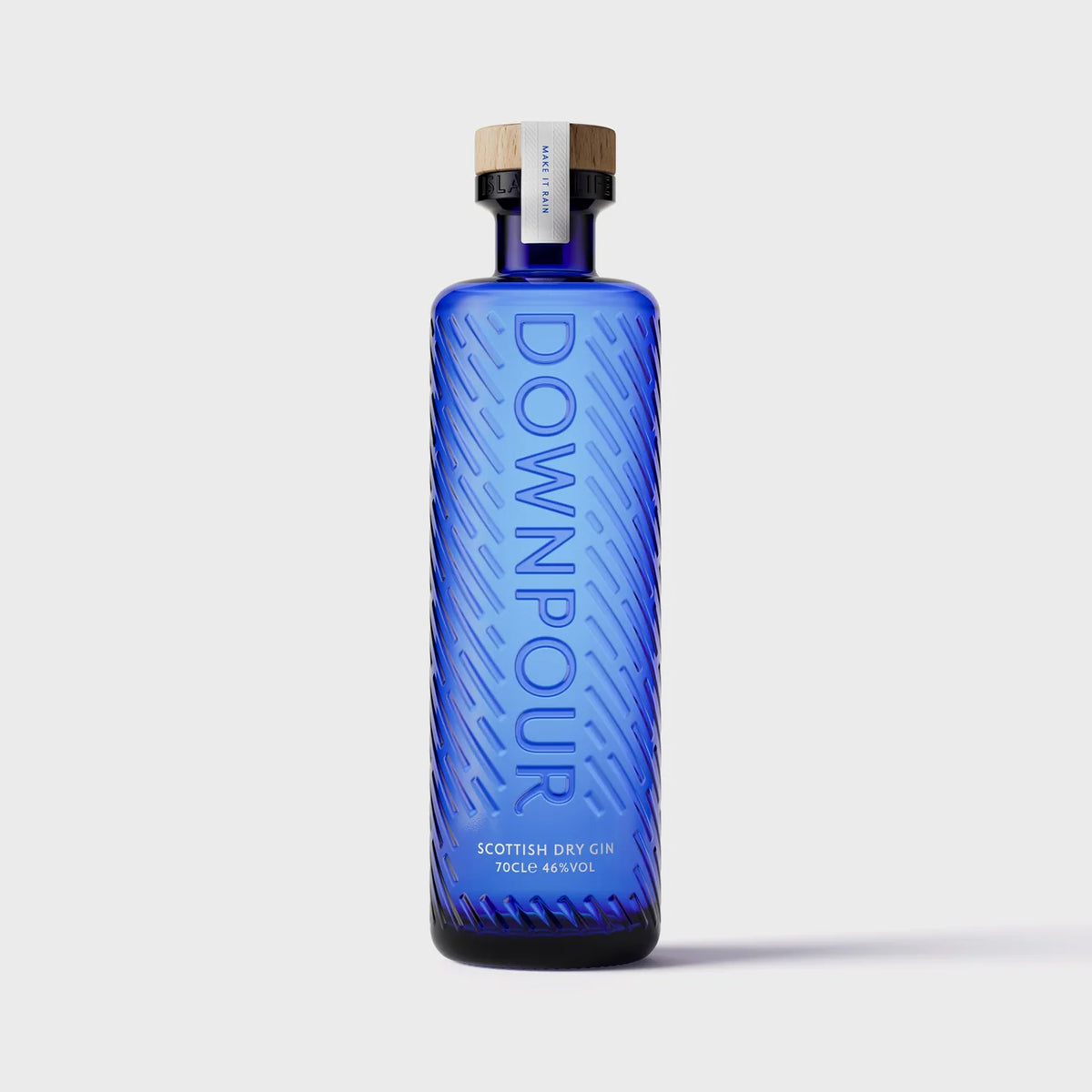 A tall, rectangular blue glass bottle of Downpour Scottish Dry Gin 70cl with a diagonal embossed texture and a wooden stopper, featuring a label that reads “DOWNPOUR” vertically.
