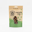 A brown and green pouch of Apple & Peanut Butter Arran Dog Biscuits, featuring a paw print logo and clear window displaying bone-shaped treats with apple inside.