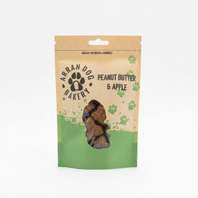 A brown and green pouch of Apple & Peanut Butter Arran Dog Biscuits, featuring a paw print logo and clear window displaying bone-shaped treats with apple inside.