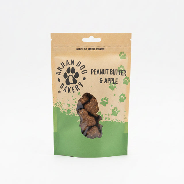 A brown and green pouch of Apple & Peanut Butter Arran Dog Biscuits, featuring a paw print logo and clear window displaying bone-shaped treats with apple inside.
